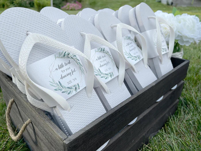 White guest thongs for beach weddings displayed in a brown basket on grass.