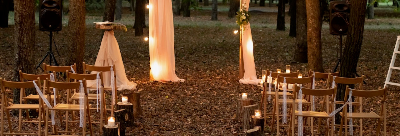 bride walking in forset that has been decorated with white paper lanterns, festoon lights and brown wooden chairs