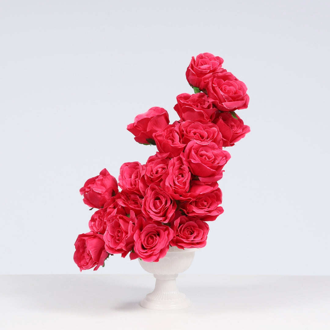 A cluster of artificial hot pink roses arranged in a white pedestal vase against a clean light gray studio background.