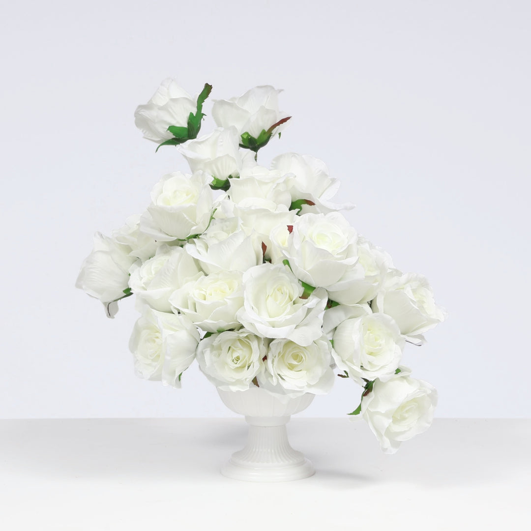 A bouquet of artificial white roses arranged in a white pedestal vase against a clean light gray studio background.