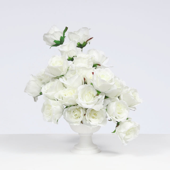 A bouquet of artificial white roses arranged in a white pedestal vase against a clean light gray studio background.