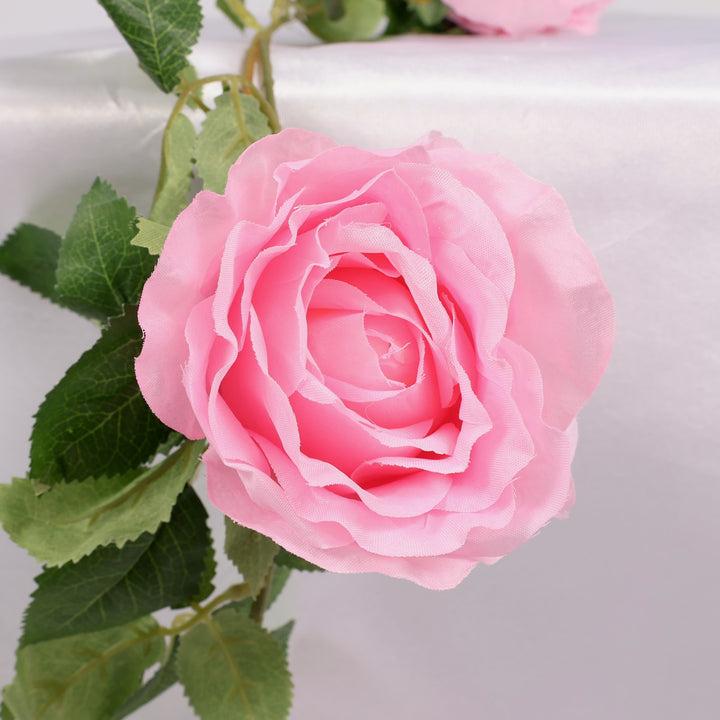 Close-up of a pink rose with green leaves on a light background