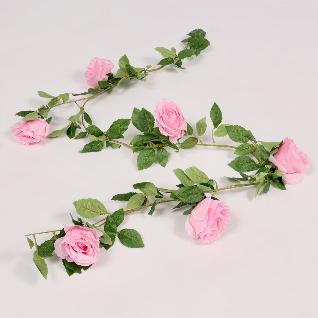 Artificial flower garland with pink roses and green leaves on a light gray background