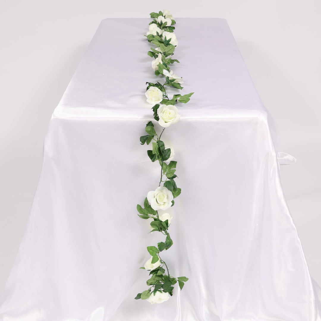 Artificial white roses and green leaves on a white tablecloth