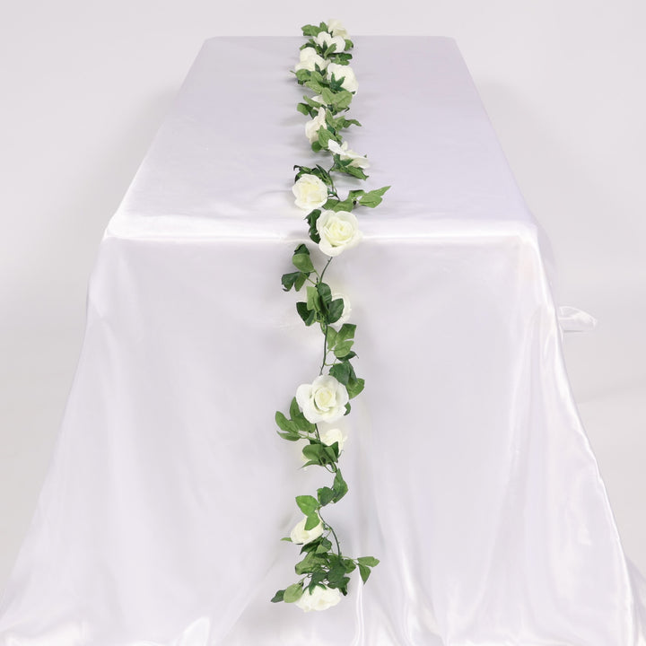 Artificial white roses and green leaves on a white tablecloth