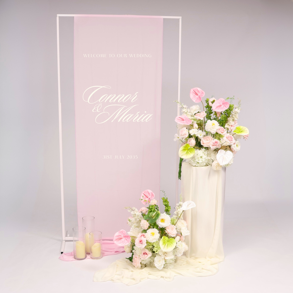 White Height Adjustable Sign, Light Pink Flower Arrangements with Anthurium Stems added, sitting on the White Round Plinth Set with Ivory Chiffon Table Runner, flickering LED pillar candles in Glass Vase Set of 3.