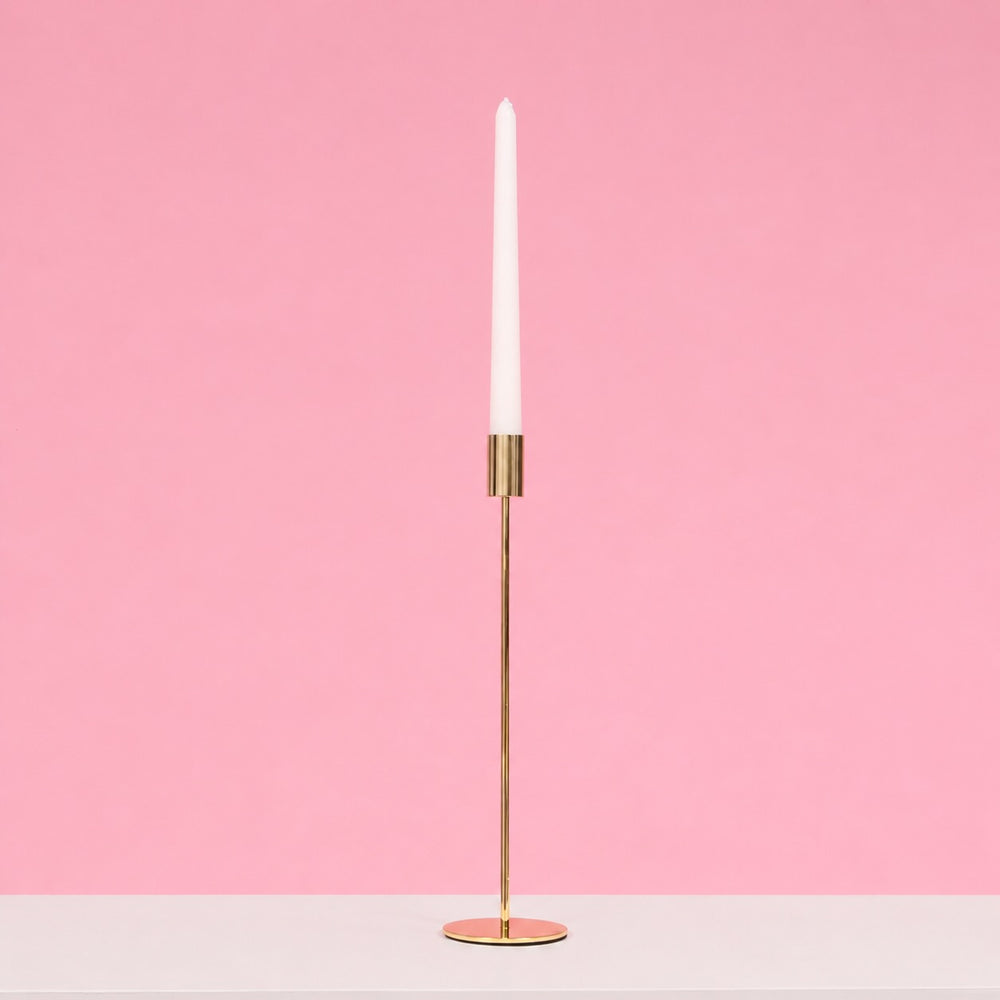 Gold candle holder with a white candle on a pink background