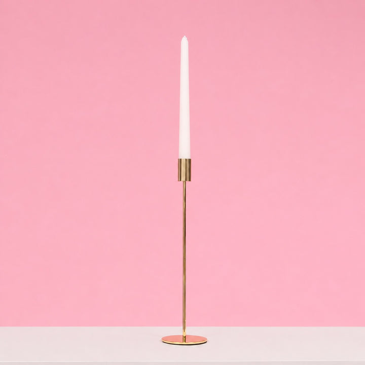 Gold candle holder with a white candle on a pink background