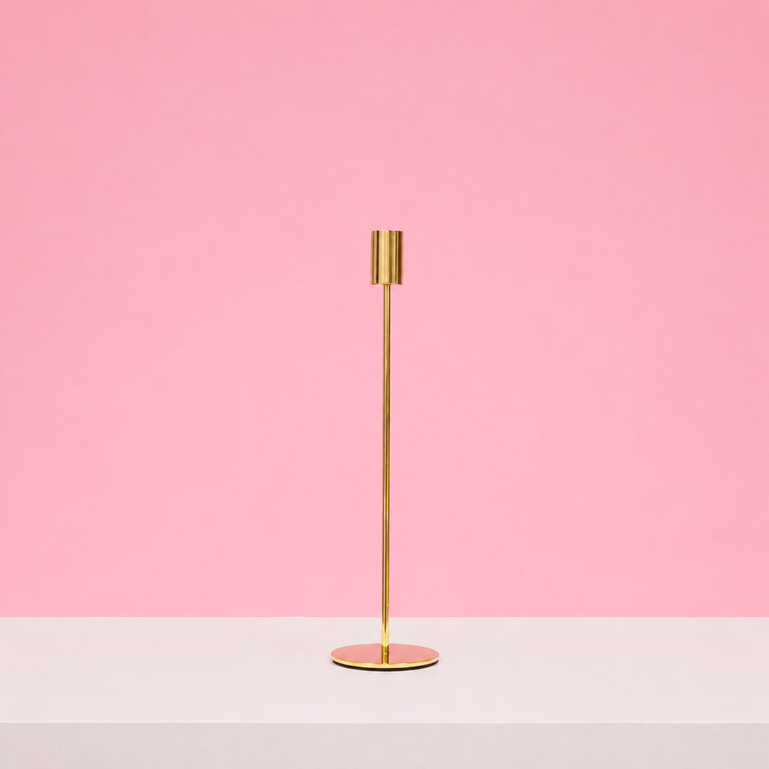 Gold candle holder on a white surface with a pink background