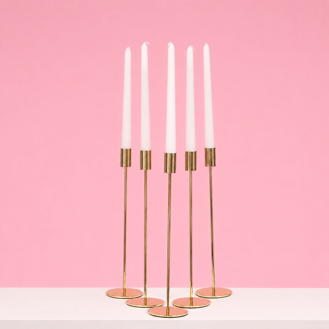 Gold candle holder with white candles on a pink background