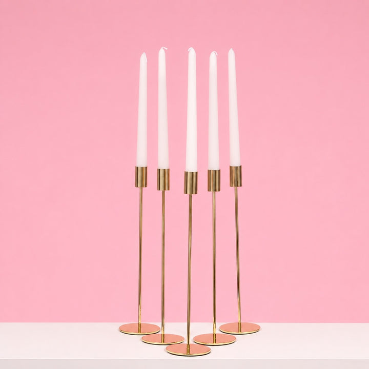 Gold candle holder with white candles on a pink background