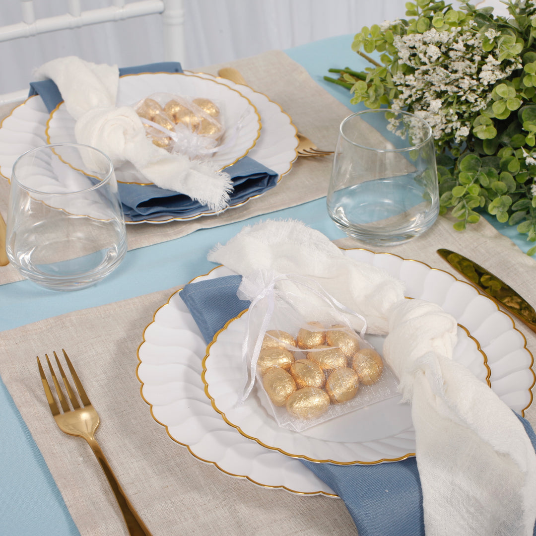 26cm shell plate with the 19cm shell plate sitting on top with dusty blue napkin, light blue tablecloth and linen placemats. Gold easter eggs sit on top of plates inside white organza gift bags