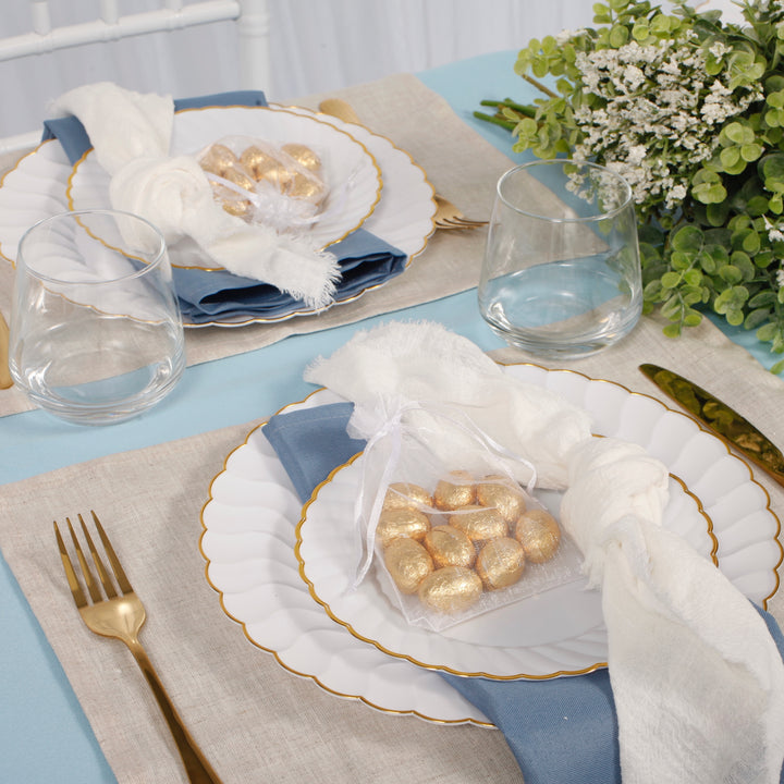 26cm shell plate with the 19cm shell plate sitting on top with dusty blue napkin, light blue tablecloth and linen placemats. Gold easter eggs sit on top of plates inside white organza gift bags