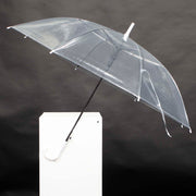 open transparent umbrella with black stem and white handle. In front of a black background on a white plinth