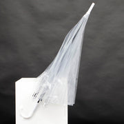 closed transparent umbrella with black stem and white handle. In front of a black background on a white plinth