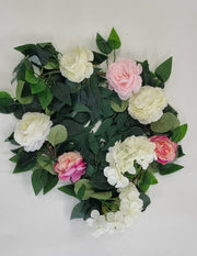 Flower garland made into a round wreath. Green leaves and foliage with large white and pink flowers and smaller pink and peach flowers.